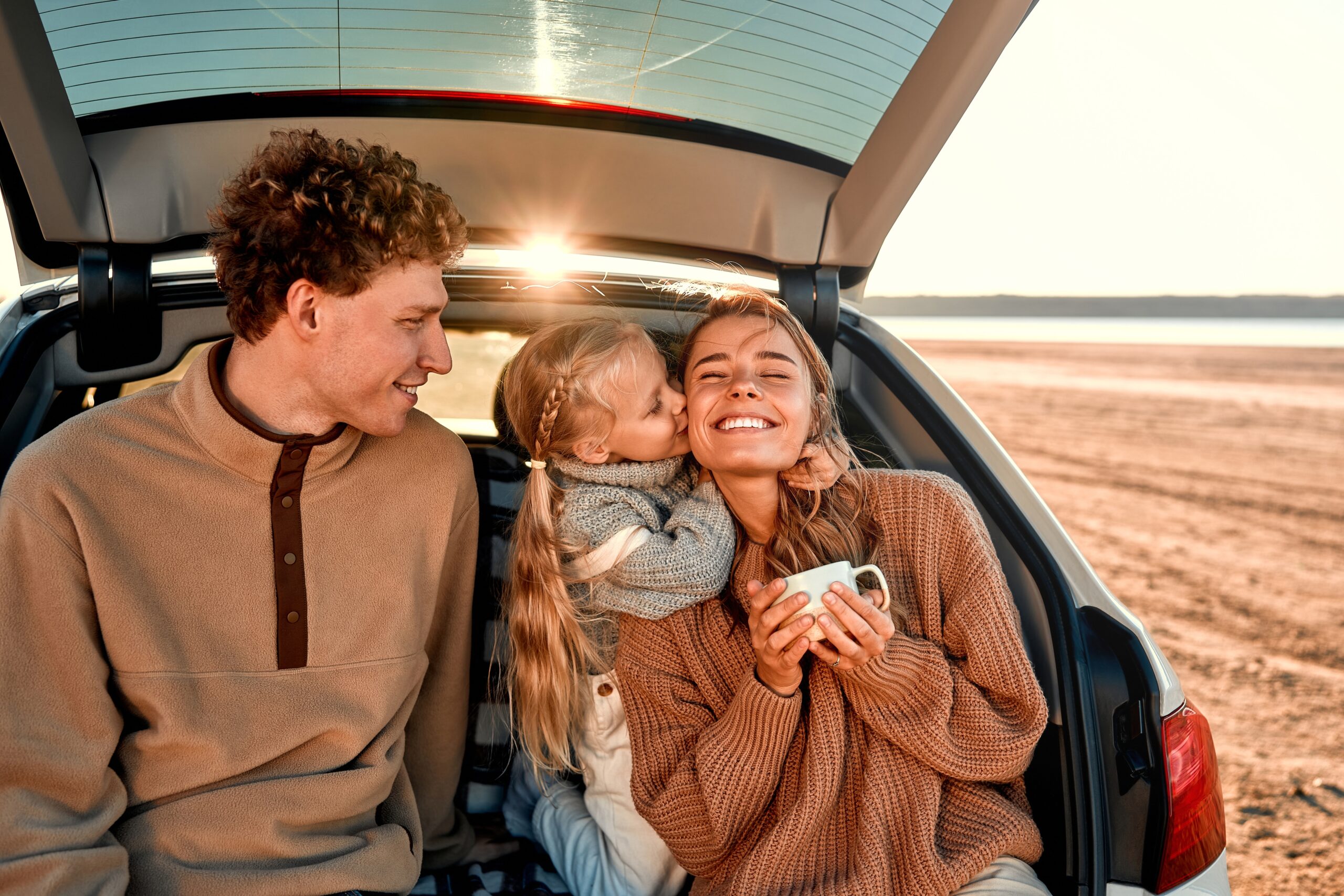 Young family sat in car on beach