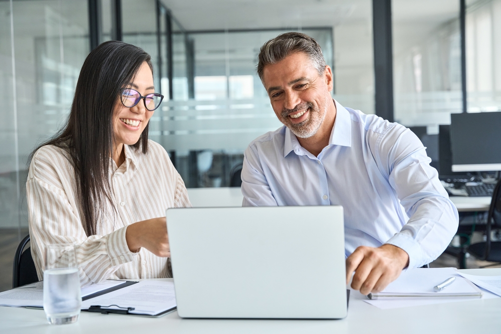 Male and female co workers smile and look at laptop in the office