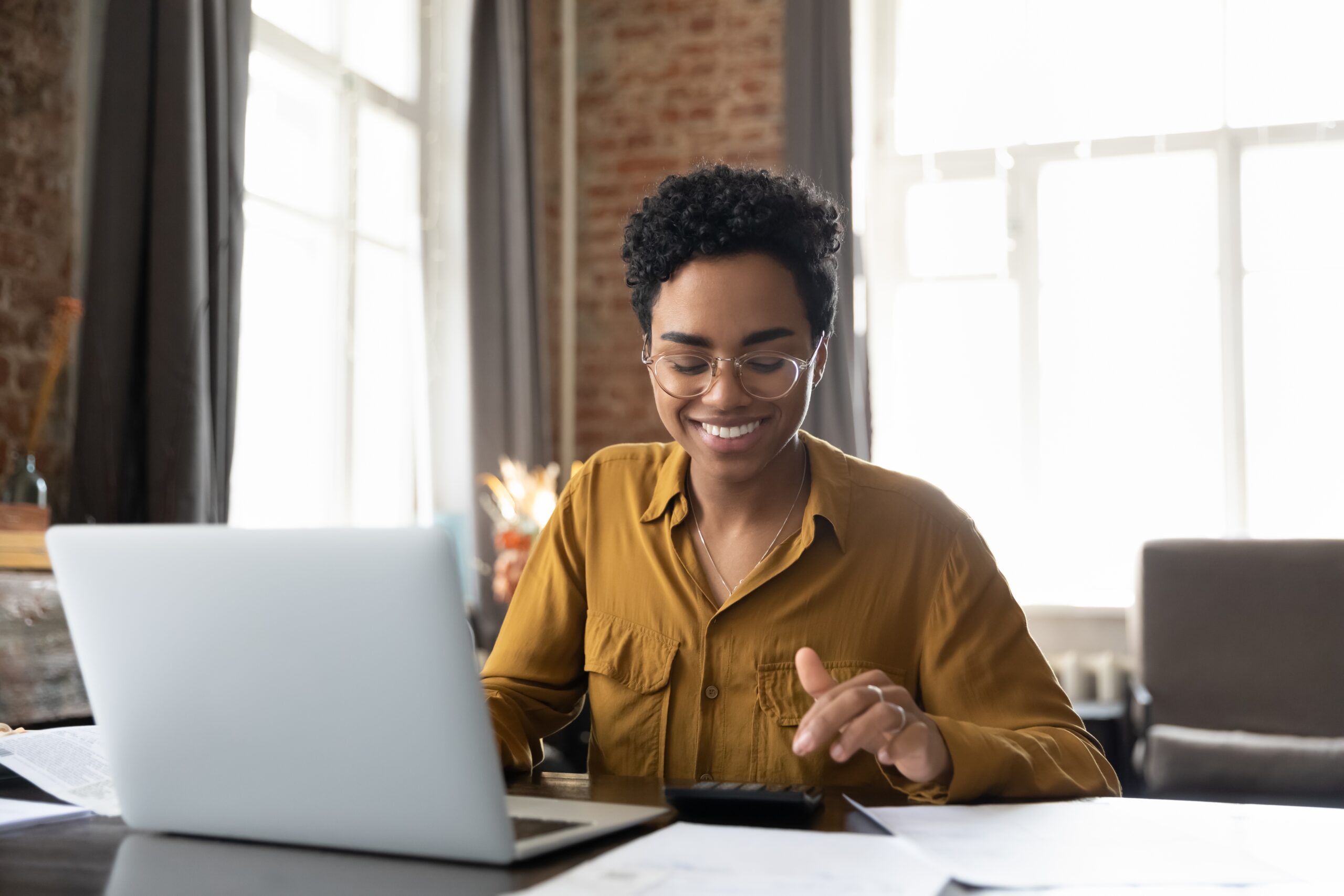 Black woman smiles while using laptop and calculator