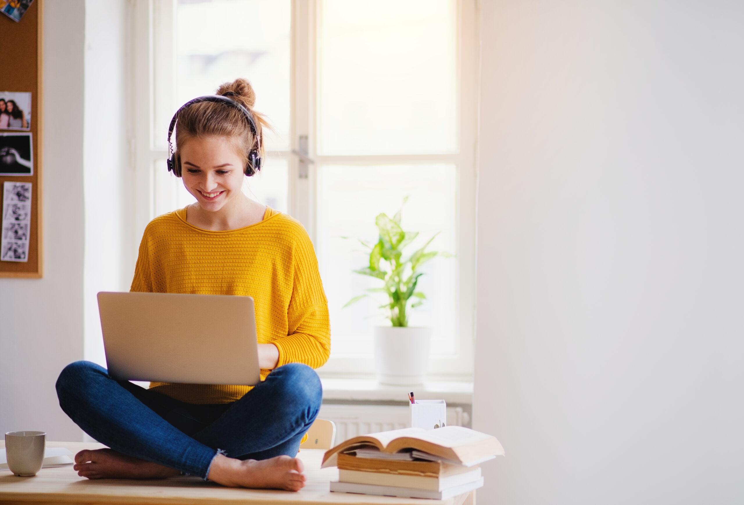 Young girl sits with headphones on looking at laptop and smiling