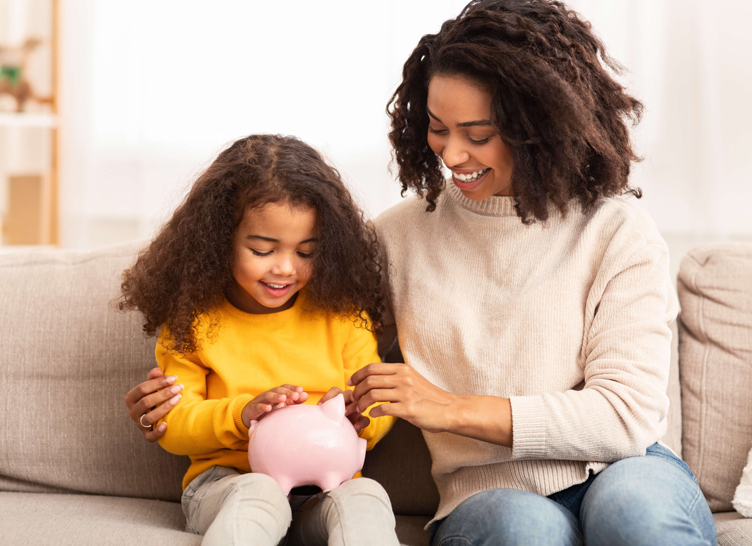 Black mother and daughter with piggy bank