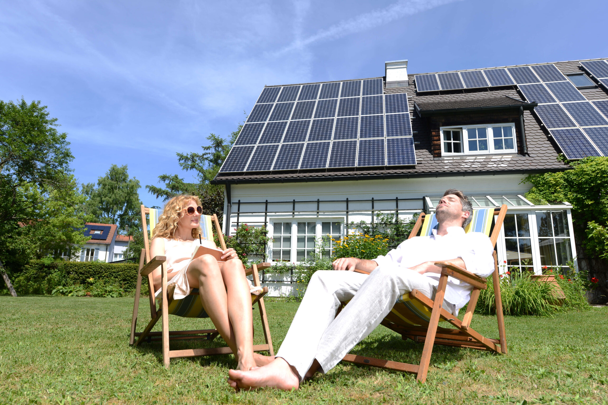 Couple lounge on sunchairs by house with solar panels