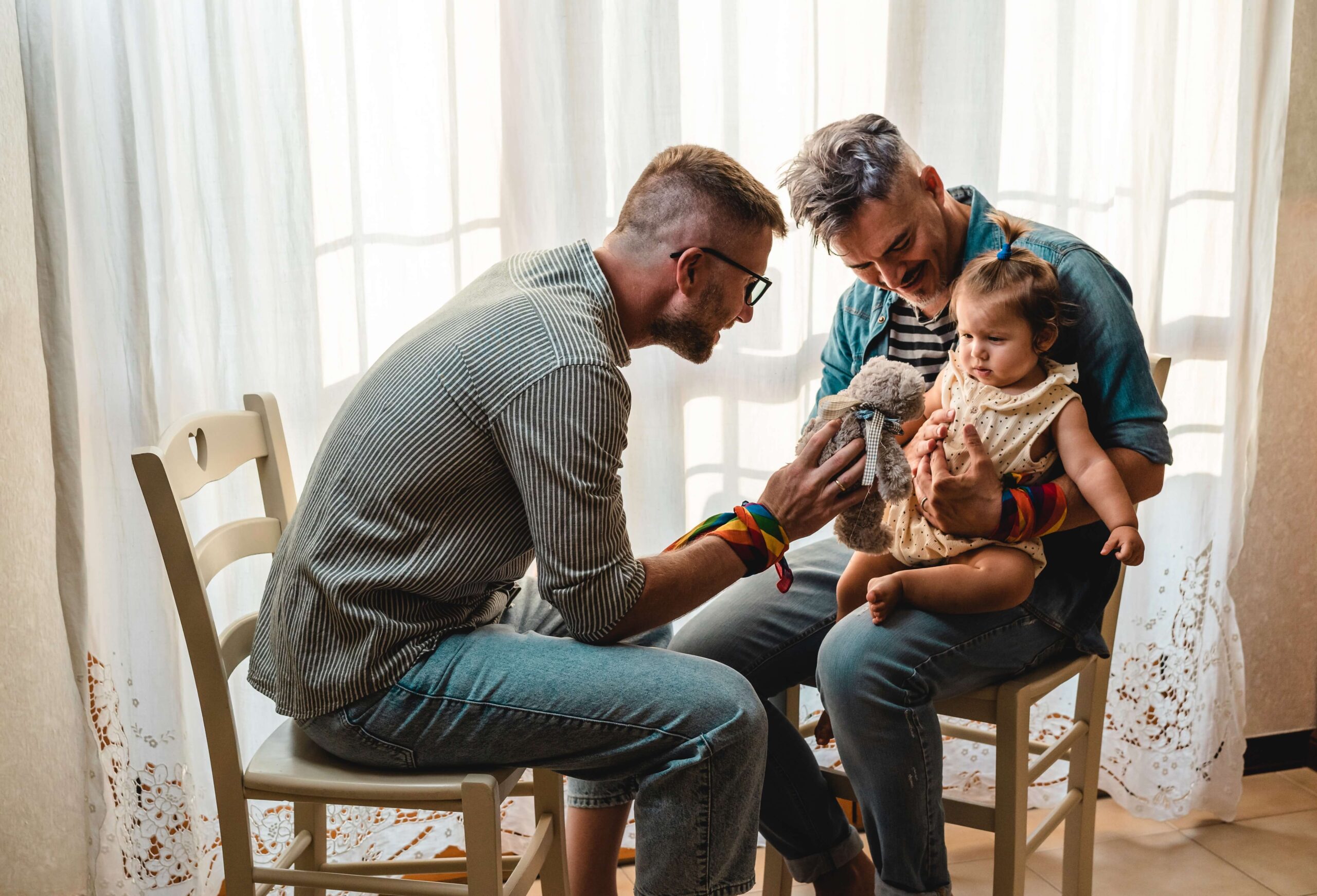 Two men with a baby and teddy bear at home