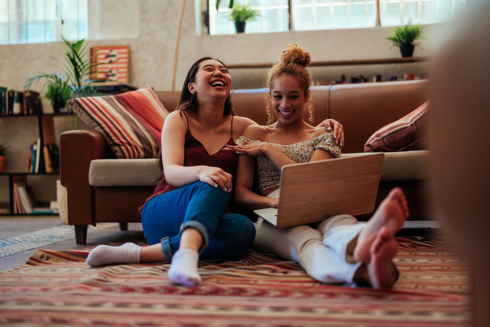 Young female friends laughing at laptop at home