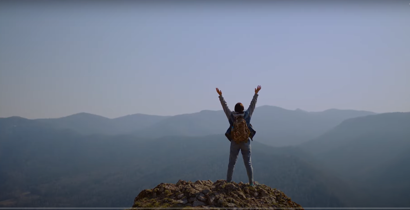 Person stands triumphantly on top of a mountain