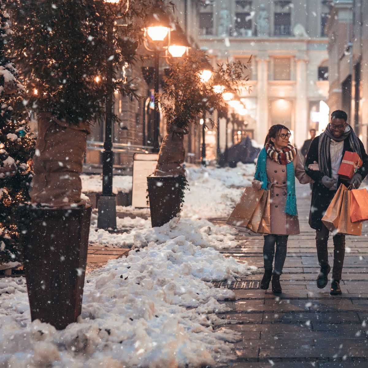 Man and woman walking down a snowy city street carrying shopping bags