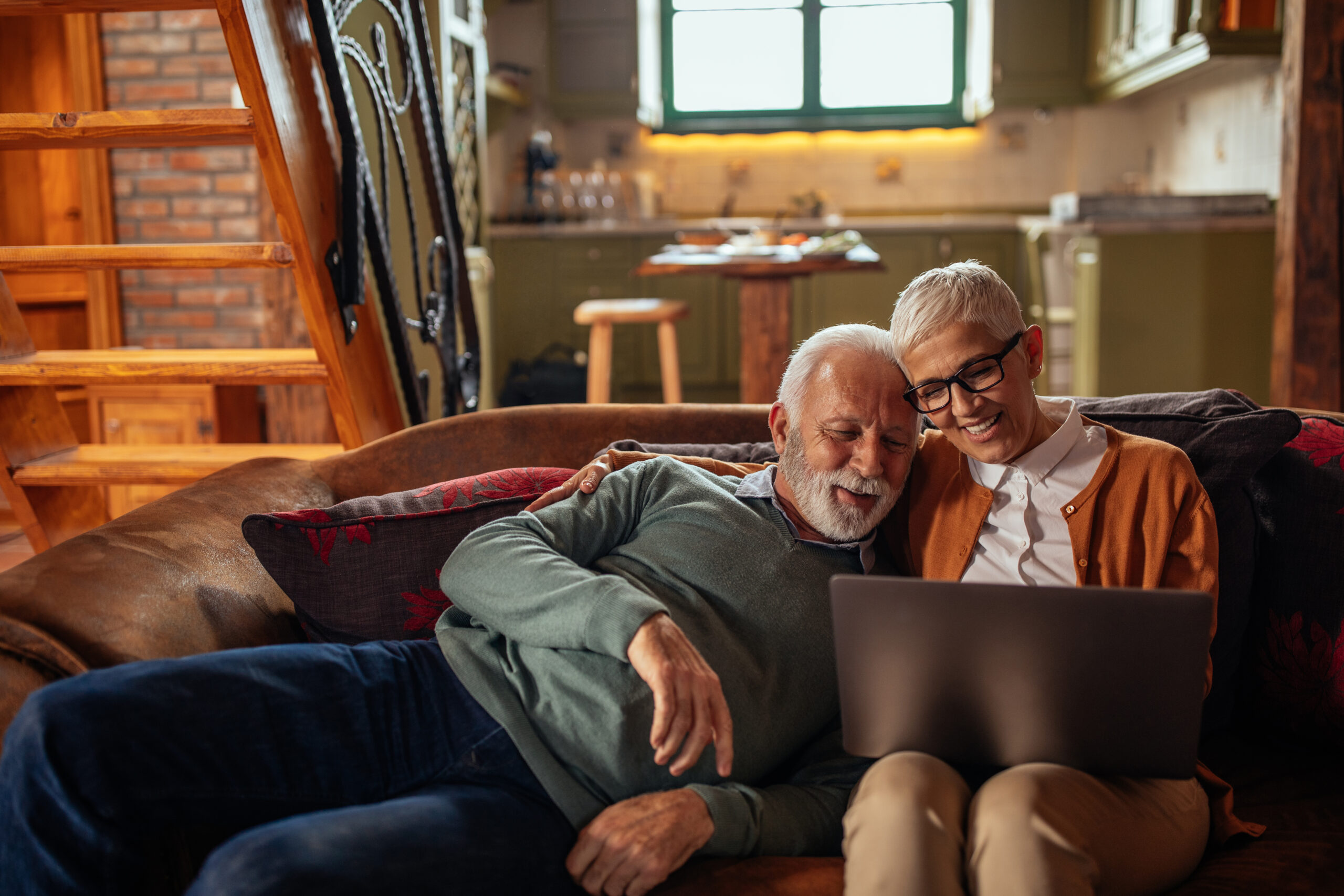 Senior couple cuddling on the sofa using their laptop
