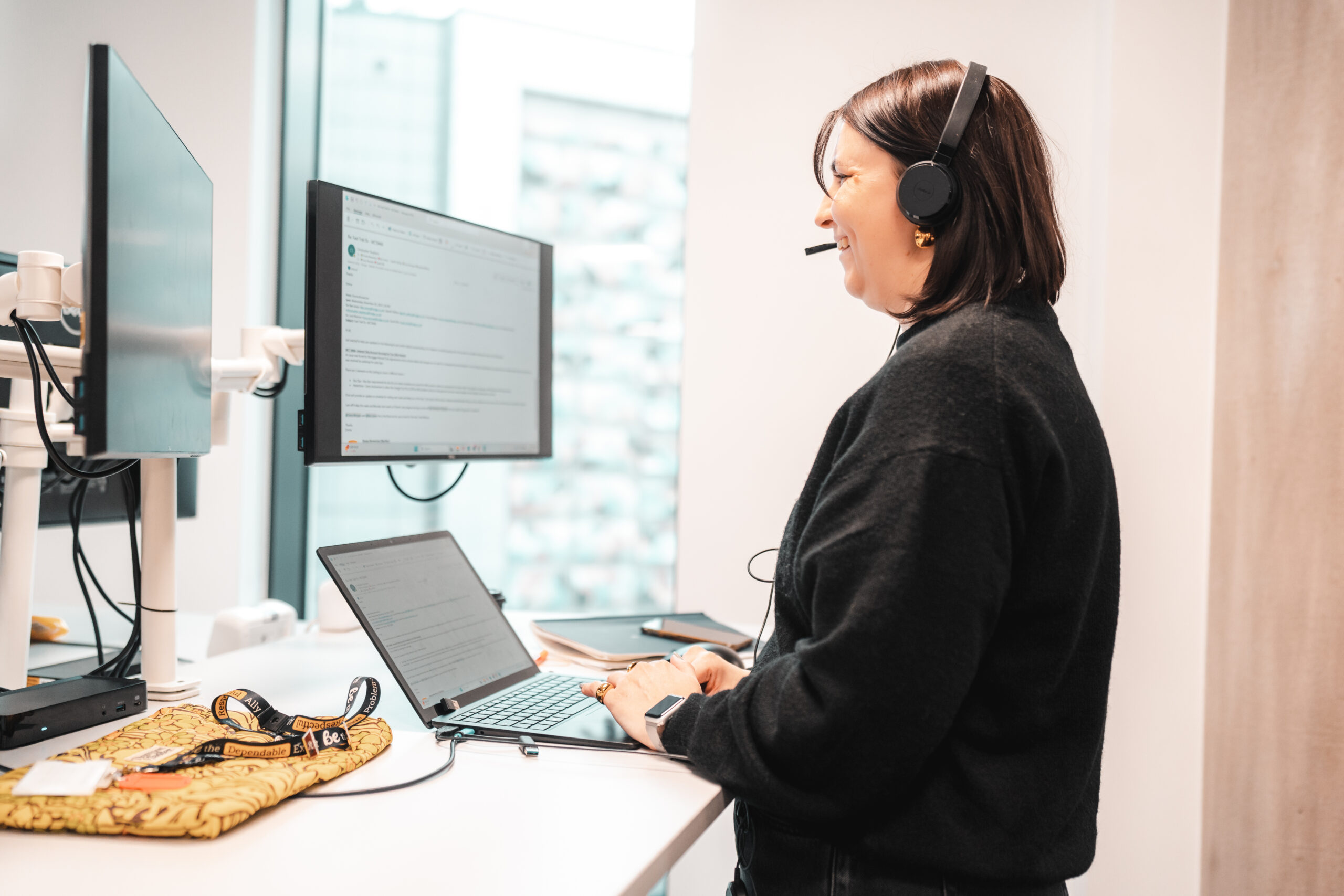 A dark haired woman smiling whilst working at her standing desk