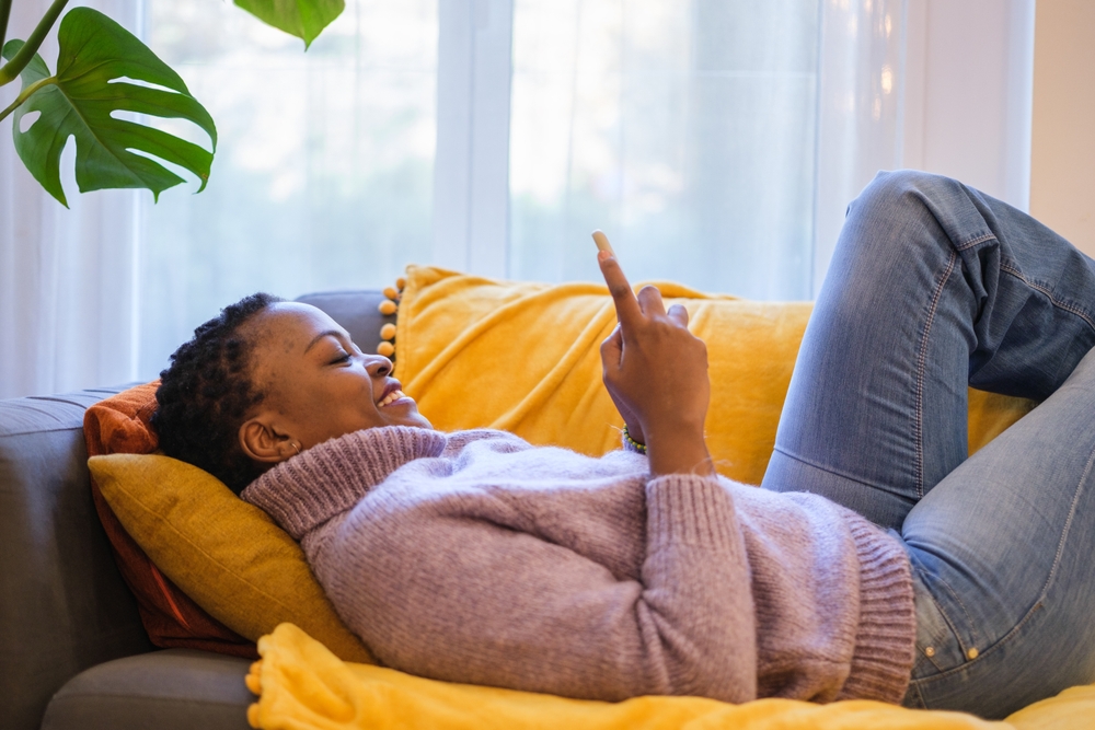 Woman lying on sofa smiling at her phone