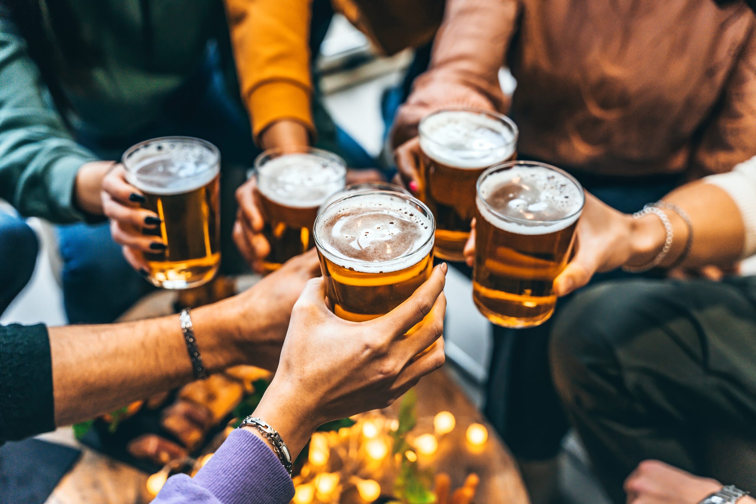 Group,Of,Friends,Drinking,And,Toasting,Glass,Of,Beer,At Five hand cheering five beers together in a pub setting