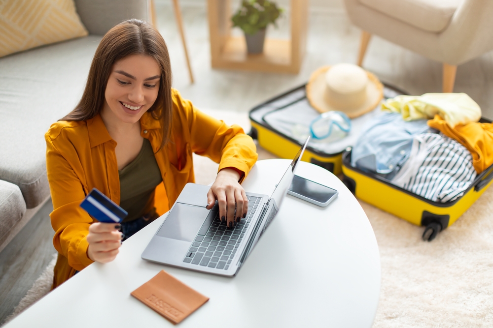 Young woman holding her credit card with a suitcase behind her