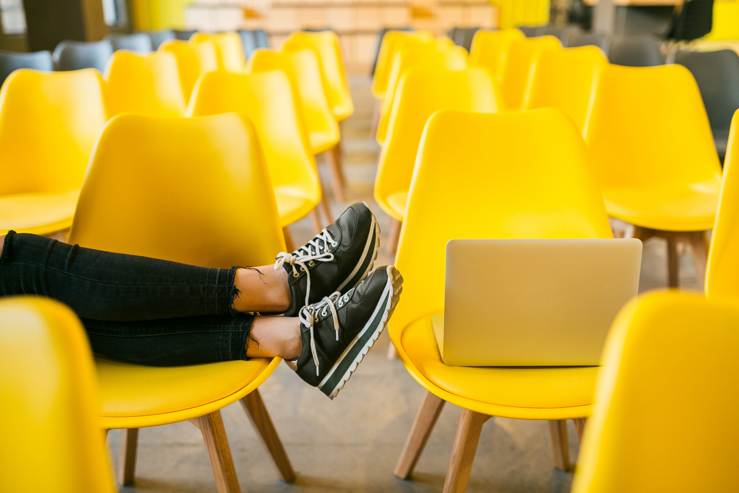 A set of yellow chairs with a pair of feet resting on them, next to a laptop.
