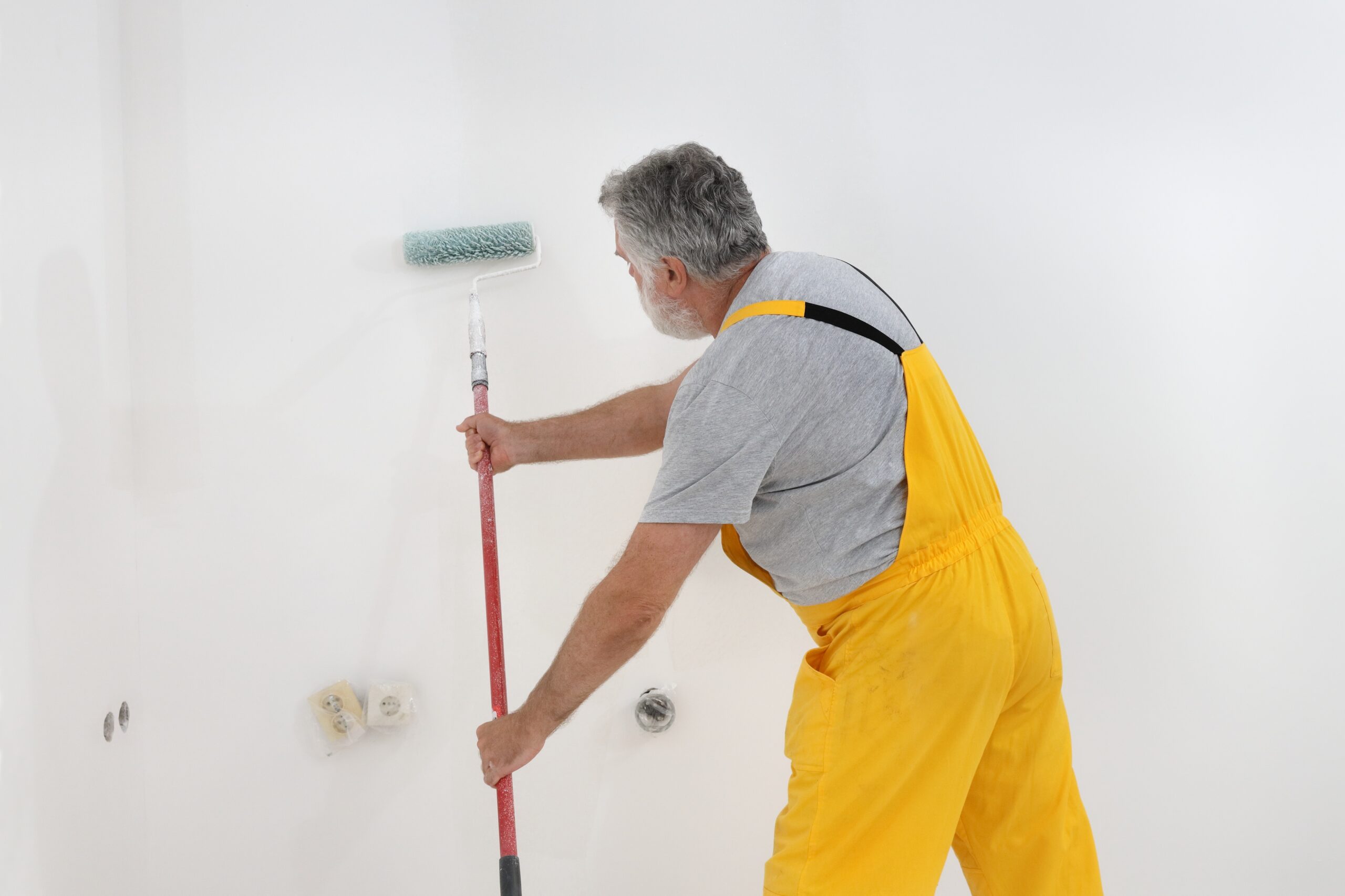 A man in yellow dungarees painting a wall.