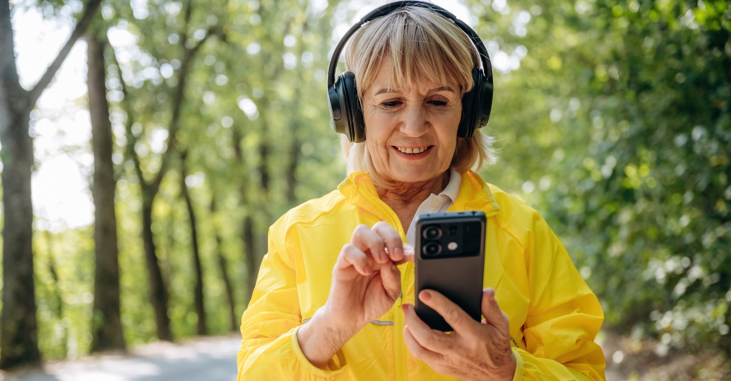 A woman wearing headphones whilst looking at her phone.