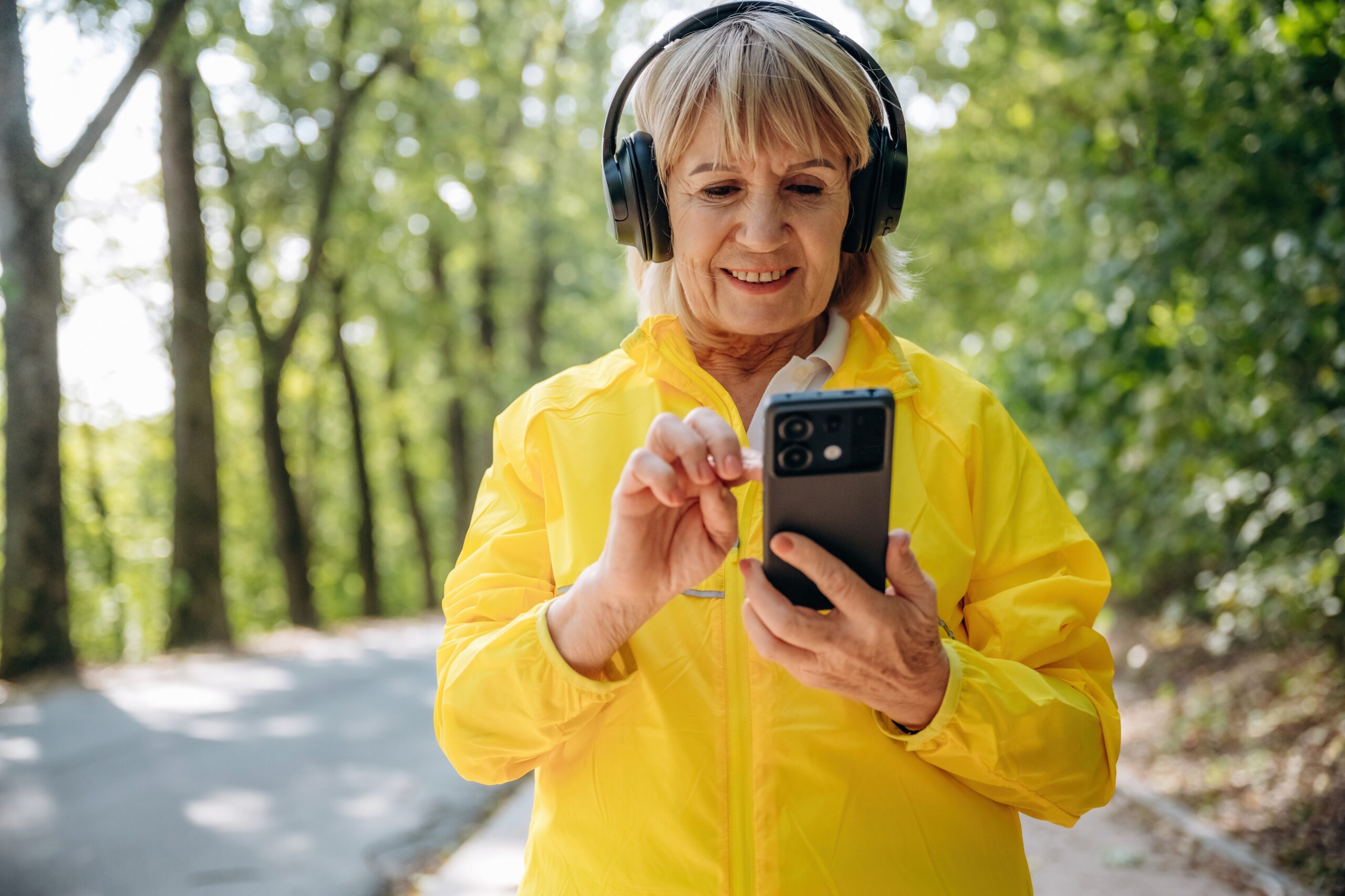 A woman wearing headphones whilst looking at her phone.