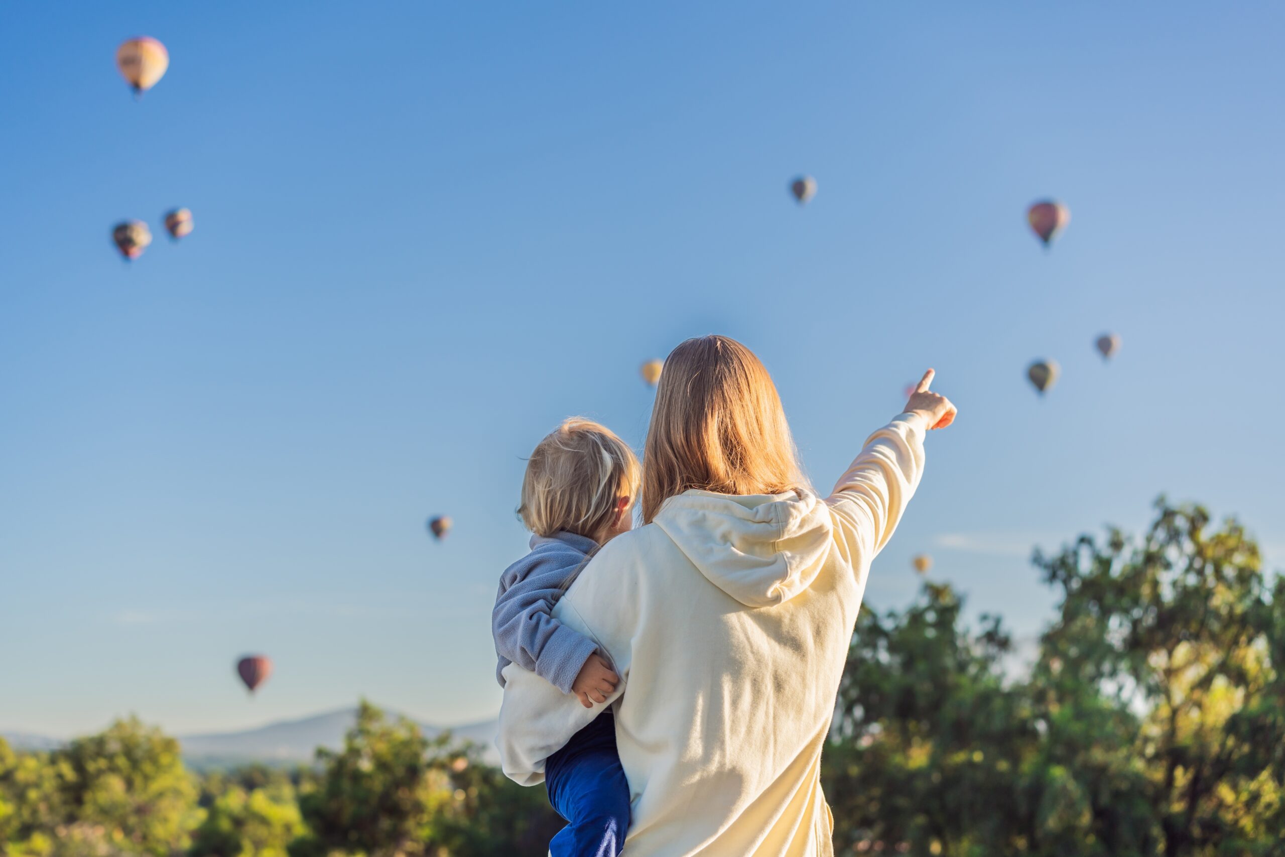 A woman holding a young child whilst pointing at balloons.