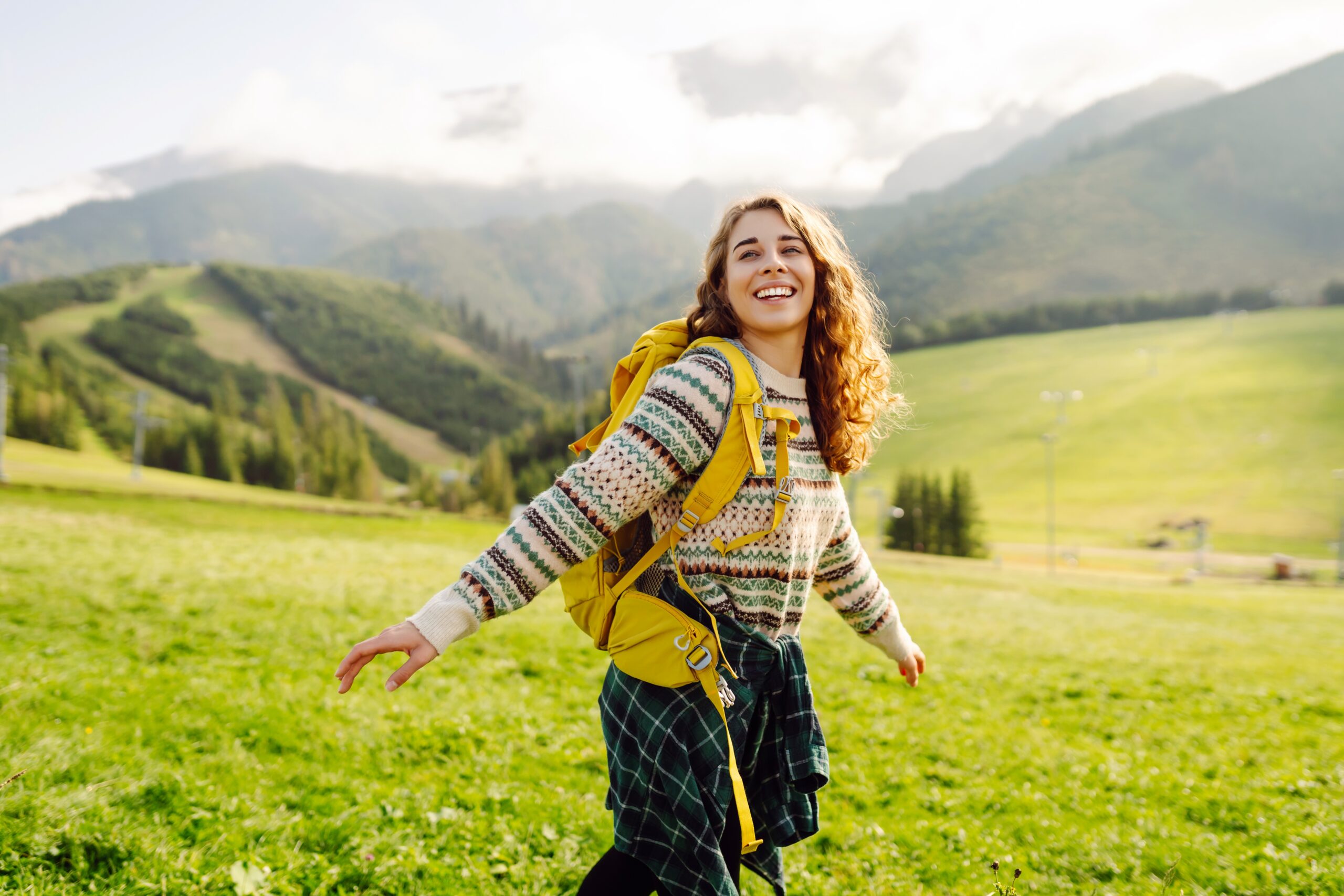 Carefree woman traveller with a backpack walks across a field in the sun with a smile on her face.